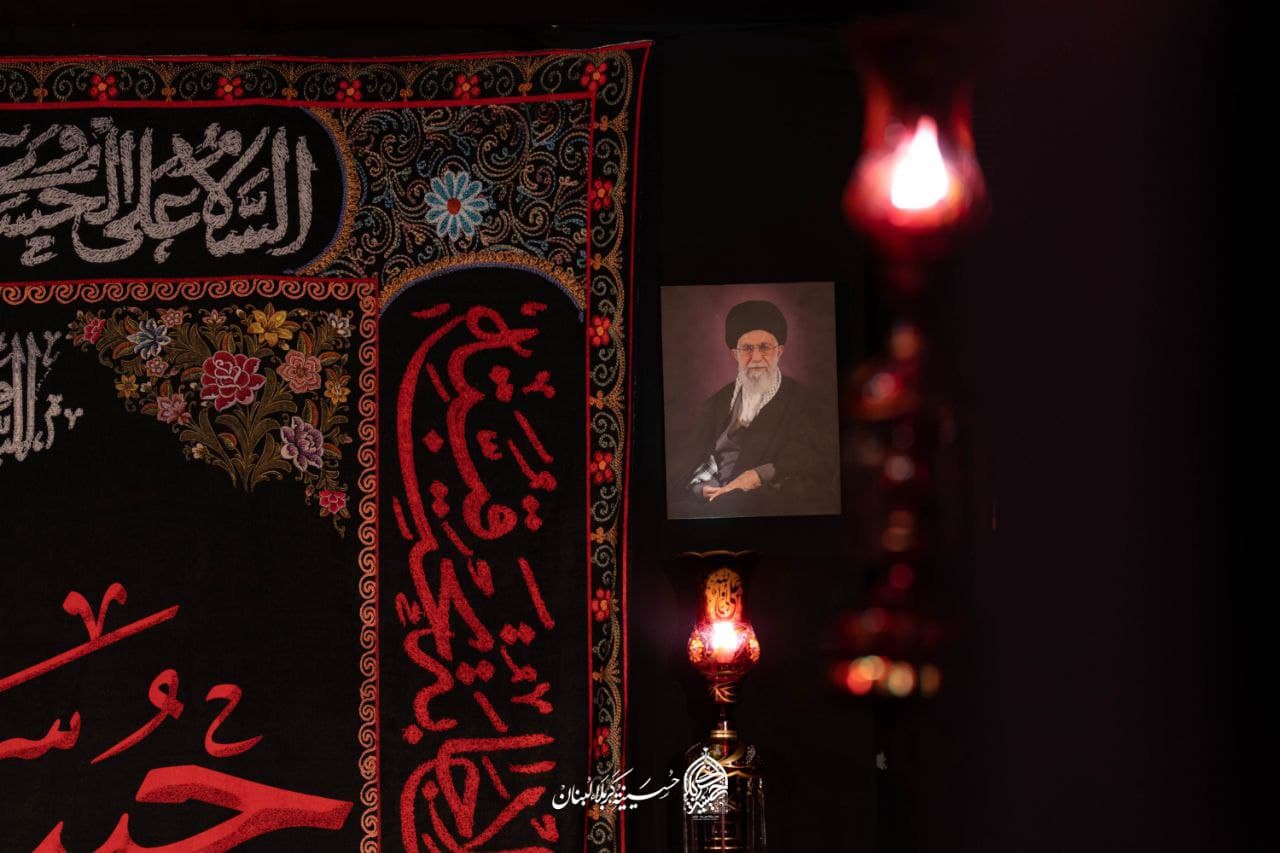 An embroidered Ashura banner with red calligraphy beside glowing lanterns